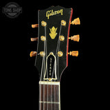 Close-up of a vintage Gibson acoustic guitar headstock, showing the gold Gibson logo, gold tuning pegs, and 'STEREO' badge on a black background.