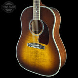 A classic acoustic guitar with a natural sunburst finish, featuring a dark brown body, bright yellow-orange center, and white binding, shown against a solid black background.