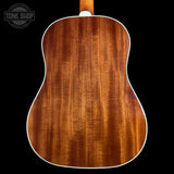 The back of an acoustic guitar made of rich, warm brown wood with a white binding edge, shown against a solid black background. A Tone Shop watermark is visible in the top left corner.