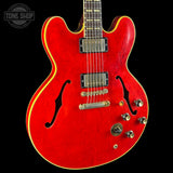 A red electric guitar with gold binding and chrome hardware, shown against a black background with a Tone Shop watermark in the top left corner.