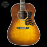 A classic acoustic guitar with a natural sunburst finish, featuring a black and brown striped pickguard and a silver-toned metal edge trim, shown against a solid black background.