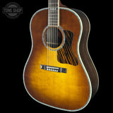 A close-up of an acoustic guitar body showing a natural sunburst finish that fades from golden yellow to dark brown, with a black pickguard and silver-toned metal tuning pegs, set against a solid black background.