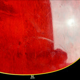 Close-up of a glossy red wooden surface with visible scratches and a bright reflection, likely part of a guitar body or similar wood product.
