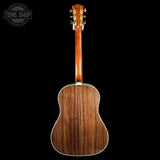 The back of a wooden acoustic guitar with a rich brown grain finish, shown against a solid black background with a Tone Shop logo in the top-left corner.