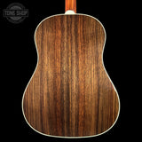 Close-up of the back of an acoustic guitar showing a rich, dark brown wood grain finish, with a white edge trim and a portion of the neck visible at the top, set against a solid black background.
