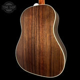 Close-up of the back of an acoustic guitar showing a rich dark brown wood grain finish with a thin white binding edge, set against a solid black background.