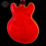 Close-up of the back of a red electric guitar body with a yellow binding edge, shown against a black background. A Tone Shop watermark is visible in the top left corner.