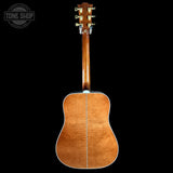 The back of a wooden acoustic guitar, showing the glossy flamed maple top and headstock, photographed against a solid black background with a Tone Shop watermark in the top-left corner.