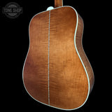 Close-up of the back of an acoustic guitar showing a rich, warm brown wood grain finish with a white binding edge, set against a solid black background.