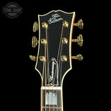 Close-up of a Gibson mandolin headstock with gold tuning pegs and strings on a black background, featuring a Tone Shop watermark in the top left corner.