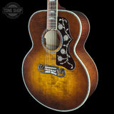 A close-up of a vintage acoustic guitar body with a natural brown sunburst finish, featuring silver floral inlays on the pickguard and a white binding around the body and neck.