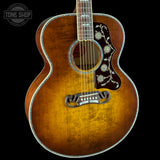 A close-up studio shot of an acoustic guitar body against a black background, showing a natural sunburst finish, floral pickguard, and bridge. A Tone Shop watermark is visible in the top left corner.