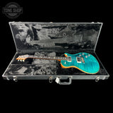 A turquoise blue electric guitar with a natural wood edge and black headstock, displayed inside an open black hard case with a black velvet interior. A Tone Shop watermark is visible in the top-left corner.