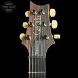 Close-up of the headstock of a Jim Marshall Tremonti acoustic guitar against a solid black background, showing the dark wood grain, gold tuning pegs, and white brand lettering.