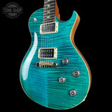 A close-up of an electric guitar body with a vibrant turquoise and teal flamed maple finish, featuring gold hardware and a black pickguard, set against a solid black background.