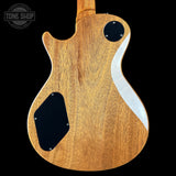 The back of an electric guitar with a natural wood finish, featuring a white wavy inlay, black pickups, and a visible Tone Shop watermark in the top left corner.