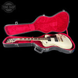 A white electric guitar resting inside an open black hard case with a bright red velvet interior, shown against a solid black background. A Tone Shop watermark is visible in the top-left corner.