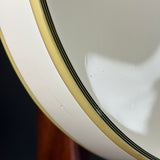 Close-up of a white ceramic bowl or plate edge with a pale yellow rim and a thin black stripe detail, photographed against a dark background.