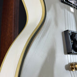 Close-up detail of an electric guitar body showing a white finish with a black and gold double-triple border, a black pickup, and a gold jack connector.