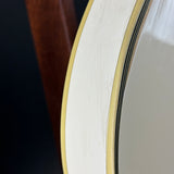 Close-up detail of a white guitar headstock edge with a gold-toned bevel and black binding, next to a dark brown wooden neck on a dark background.