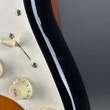 Close-up detail of an electric guitar body showing a cream pickguard, cream control knobs, a glossy black edge, and part of a warm brown wood finish against a dark gray background.