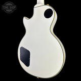 The back of a white electric guitar with gold trim and black hardware, shown against a solid black background with a Tone Shop watermark in the top left corner.