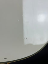 A close-up of a white curved surface with a small water droplet and minor scuffs, photographed against a dark background.