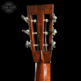 Close-up of the headstock of a wooden acoustic guitar against a solid black background, showing six tuning pegs and strings. A Tone Shop watermark is visible in the top-left corner.