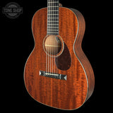 A close-up studio shot of an acoustic guitar body with a rich reddish-brown wood grain finish, featuring a dark pickguard, silver bridge, and part of the neck against a solid black background. A 'TONE SHOP' watermark is visible in the top-left corner.