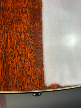Close-up detail of an acoustic guitar's wooden body, showing a glossy dark brown wood finish with prominent grain and a thin gold-toned edge stripe.