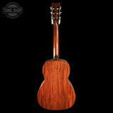 The back of a wooden acoustic guitar, showing the rich grain of the mahogany-toned wood, photographed against a solid black background with a Tone Shop watermark in the top-left corner.