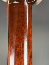 Close-up of a polished reddish-brown wooden object, showing the wood grain and a glossy finish against a neutral gray background.
