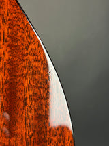 Close-up of a glossy reddish-brown wood surface with visible grain and a curved edge against a dark gray background.