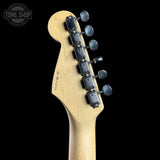 Close-up of the headstock of a guitar with a natural wood finish and six black tuning pegs, shown against a solid black background with a Tone Shop watermark in the top left corner.