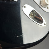 Close-up of a glossy black electric guitar body with a chrome oval pickguard and part of a cream control knob visible.