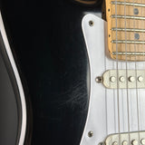 Close-up of an electric guitar body showing a black glossy finish, white pickguard, silver hardware, and part of a light wood fretboard.
