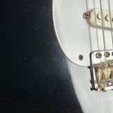 Close-up of a black electric guitar body with a white pickguard, showing part of the bridge, strings, and hardware.