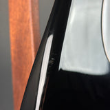 Close-up of a glossy black curved surface with a vertical white highlight and a blurred brown vertical element in the background.