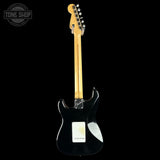 A black electric guitar shown from the back against a solid black background, featuring a natural maple neck and a white pickguard.