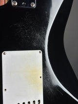Close-up of a black electric guitar body with a white pickguard showing yellowed age-related discoloration and visible surface scratches.