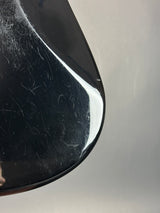 Close-up of a glossy black curved surface with visible scratches and scuffs, photographed against a plain light gray background.