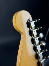 Close-up of the headstock and tuning pegs of an electric guitar, showing a natural wood finish and silver metal hardware against a dark background.