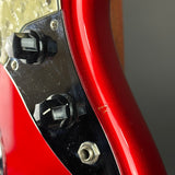 Close-up of a red electric guitar body showing a black control plate with black knobs and a metal input jack, photographed against a neutral gray background.