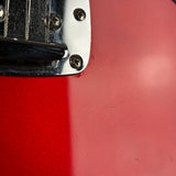 Close-up of a red electric guitar body with a chrome hardware piece and screws, showing minor scuffs on the glossy finish.