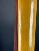 Close-up of a glossy yellow wood surface with visible grain and a small circular defect, next to a darker brown wood edge against a dark background.