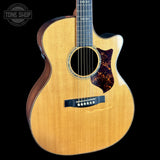 Acoustic guitar with a tortoiseshell pickguard on a black background, featuring the Tone Shop logo.