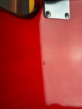 Close-up of a glossy red guitar body with a silver metal plate and two screws, showing a small dent on the red surface.