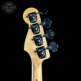 Close-up of a bass guitar headstock with a natural light wood finish and four black tuning pegs, shown against a solid black background with a Tone Shop watermark in the top left corner.