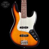 A classic four-string bass guitar with a sunburst finish, featuring a white pickguard and black control plate, shown against a solid black background with a Tone Shop watermark in the top left corner.