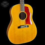 A close-up of an acoustic guitar body with a natural wood finish, a red pickguard, and a black bridge, shown against a black background with a Tone Shop watermark in the top left.